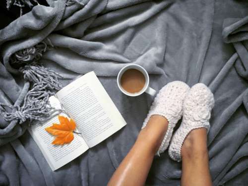 *NOMINATED* Flay lay of cozy fuzzy slippers with a book open and coffee on top of a cozy warm gray blanket. 