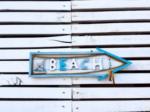 Arrow beach sign on a white wooden wall
