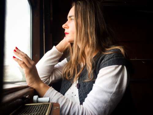 Woman in train sitting next to the window and looking outside with a hand on the window