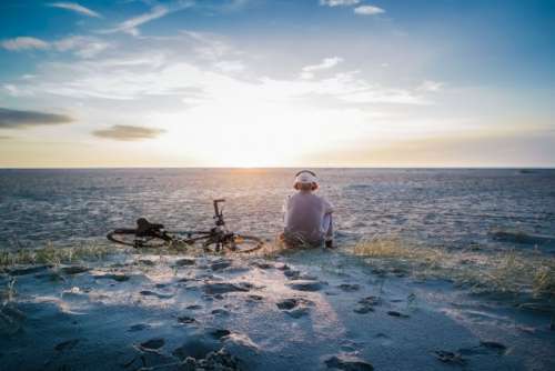 Young man sitting on the beach listen to Some music thruw his headphone and next to HIM lay his bike