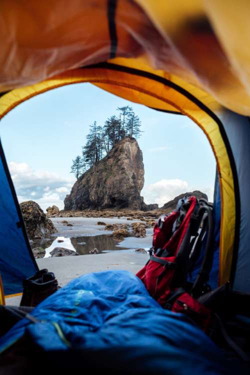 Looking out a tent, over a sleeping bag, boots, backpack and looking out at sunrise on the washington coast