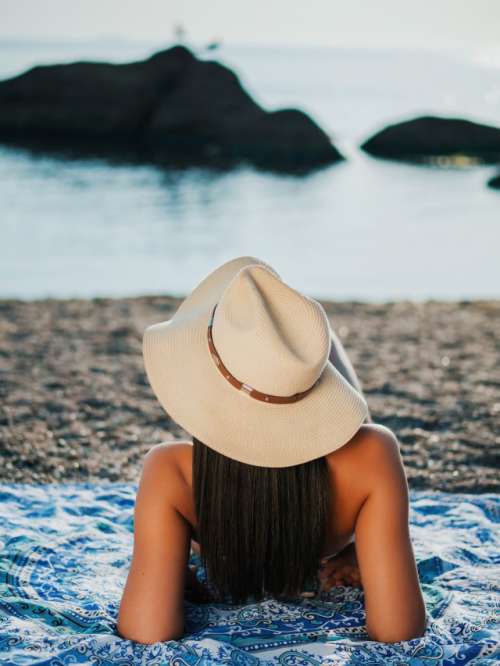 Girl in hat lying on beach near sea 