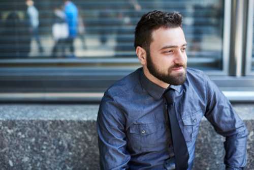 Young bearded Brazilian man relaxes on a bench in the Financial District in New York City
