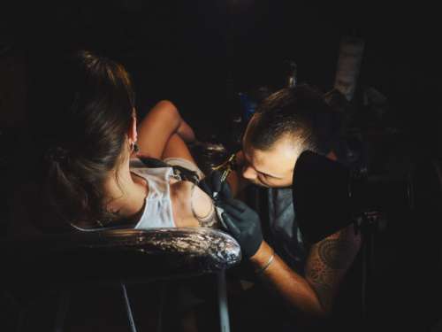 Tattoo artist making ink tattoo to young woman in studio