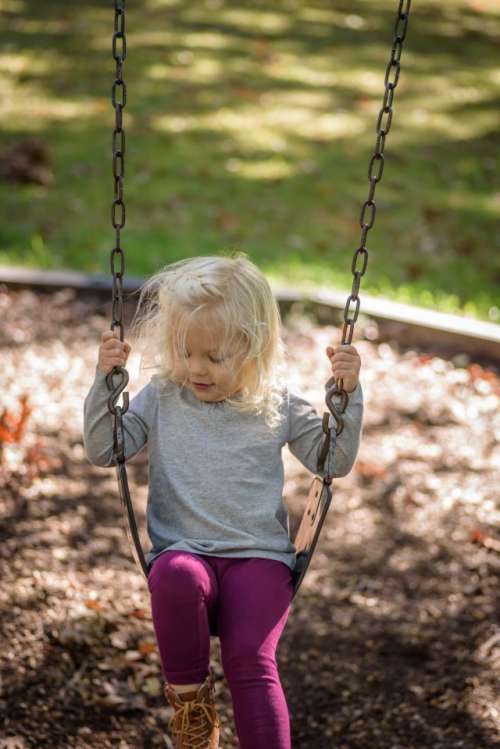 Happy girl playing on swing at playground in fall