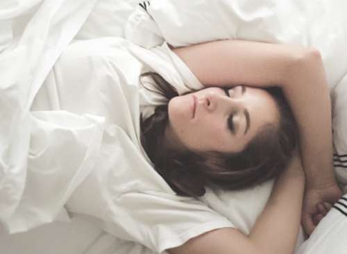 Young woman sleeping in bed with white sheets