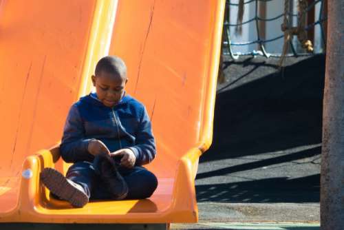 Little African boy tying his shoelace on a slide at the V&A Waterfront, Cape Town