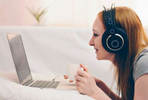 Girl listening music in headphones on a white bed.