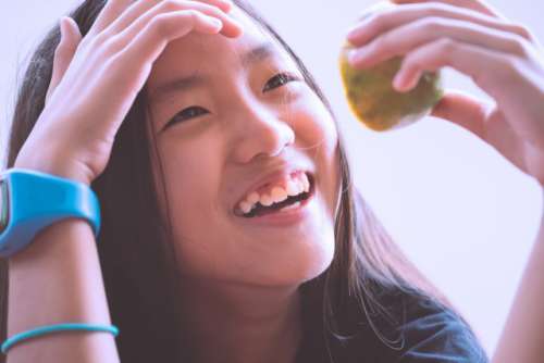 Overhead shot of an asian girl smiling happily while holding half sliced orange in her hand