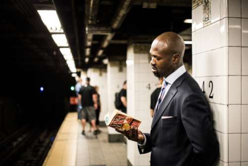 commute - man reading book at subway station 