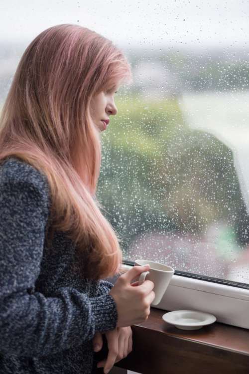girl looks out the window in rainy weather