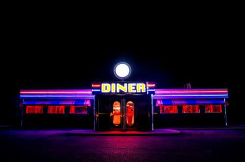 A traditional American Diner at night with a large sign and clorful luminous, fluourescent and neon lighting that glows in the dark.