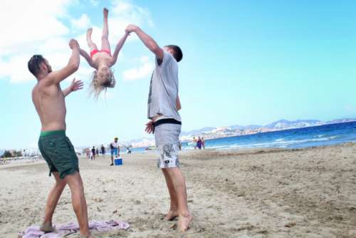 2 guys swinging a girl on the beach