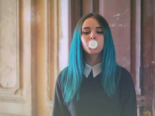 Portrait of Young girl with blue hair blowing bubble 