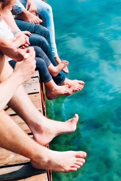 Close shot of legs family spending time together sitting on jetty over the lake in the summertime