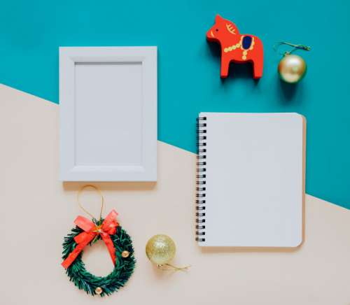Creative flat lay of craft and photo frame, blank notebook mock up with christmas ornaments and gift box on colorful background, minimal style