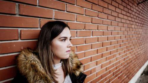  Urban portrait of a young woman in front of a brick wall. Young millenial in a winter jacket. 