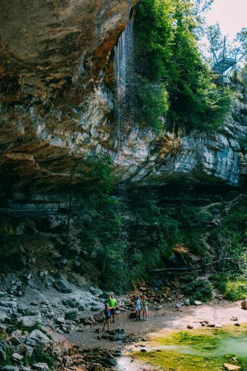 Hikers Under A Rocky Outcrop And Small Waterfall Photo