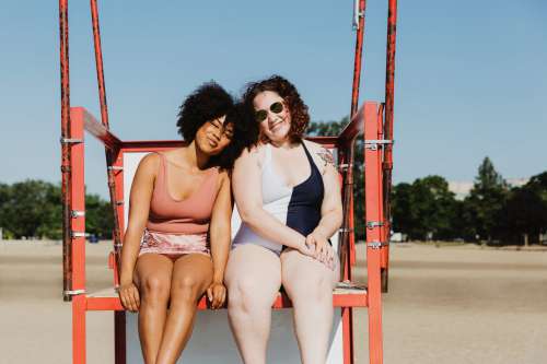 Two Women Sitting On Red Metal Lifeguard Chair At Beach Photo
