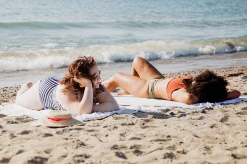 Two Women Laying On Sandy Beach On Sunny Day Photo
