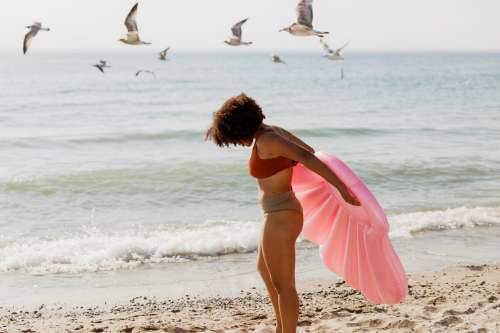 Woman Standing On Beach Holding Pink Inflatable Shell Toy Photo