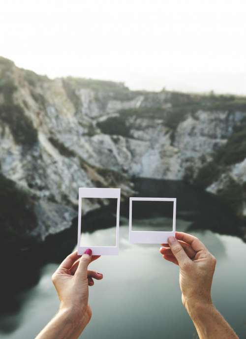 Hands holding a photo frame shaped paper cut out templates in front of mountains