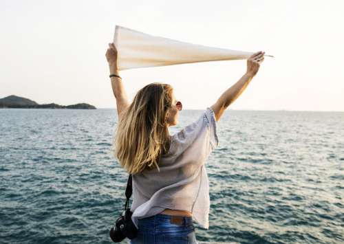 A young woman holding white flag high at a seashore