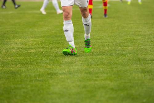Footballer legs and green shoes on ground