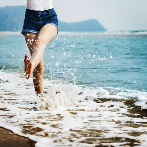 A young woman s legs splashing water on the beach