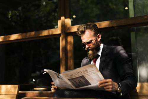 A bearded man wearing sunglasses reading a newspaper