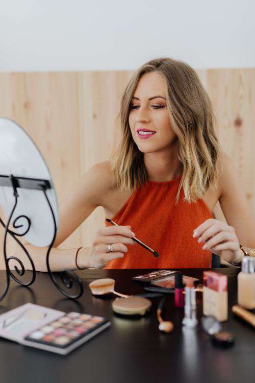Young woman sitting and doing makeup in front of mirror