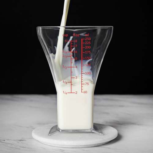 A Stream Of Milk Pours Into Triangle-shaped Measuring Glass Photo