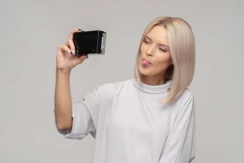 Young Woman Taking A Selfie With An Old Camera And Showing A Tongue