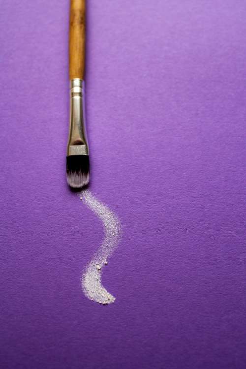 A Paintbrush Trails White Paint On Purple Paper Photo