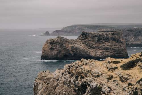 A Big Stone Outcrop Stands Apart From Cliffs In The Grey Sea Photo