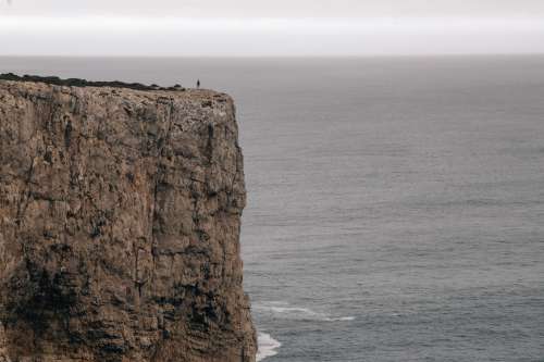 A Figure On A Cliff Overlooking The Ocean Under A Grey Sky Photo