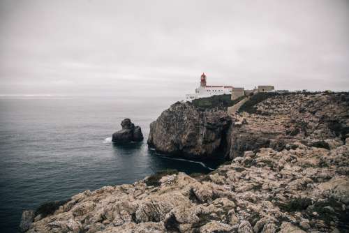 A White-Wash Lighthouse Stands On A Craggy Cliff Photo
