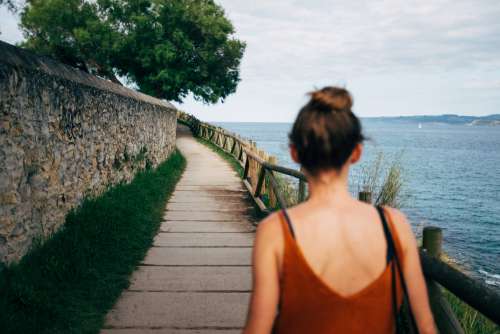 A Woman In A Summer Top Strolls Along A Footpath By A Bay Photo