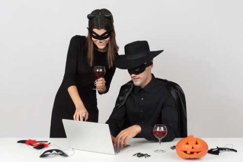 Woman In Cat Costume And Her Coworker In Zorro Costume Looking At Something At Notebook