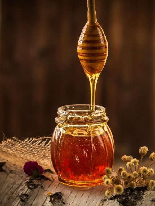 Honey dripping from dripper into the glass jar