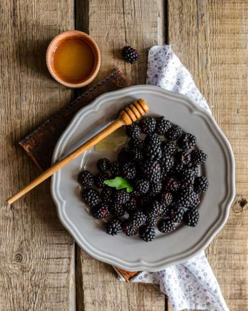 Overhead view of blackberries and honey in a ceramic plate