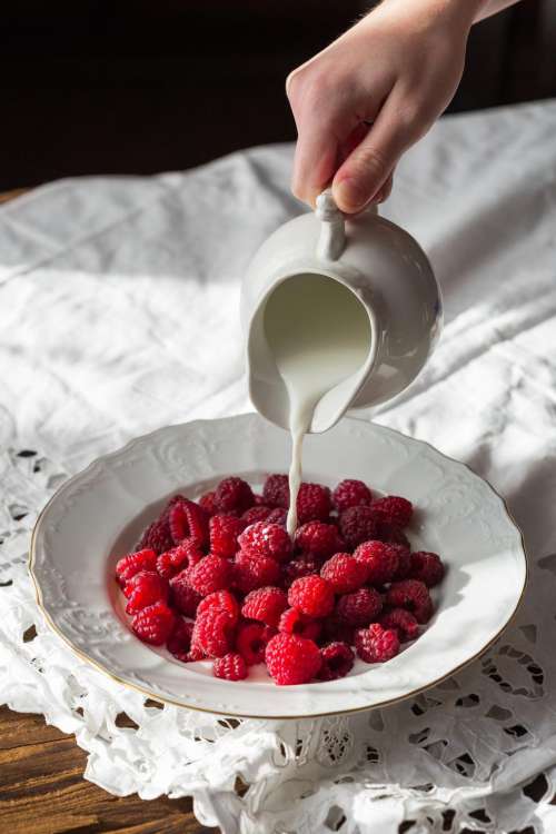 Close up milk being poured into a plate full of raspberries