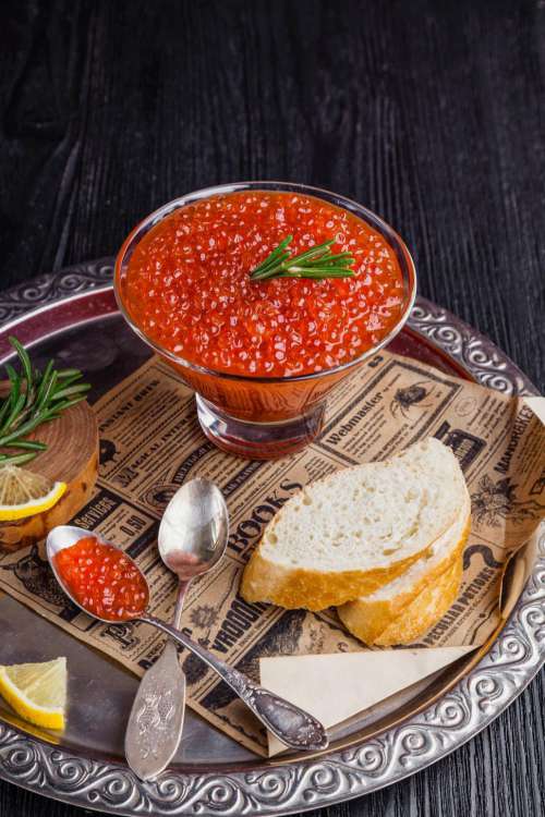 Close up of a bowl of red caviar garnished with rosemary leaves