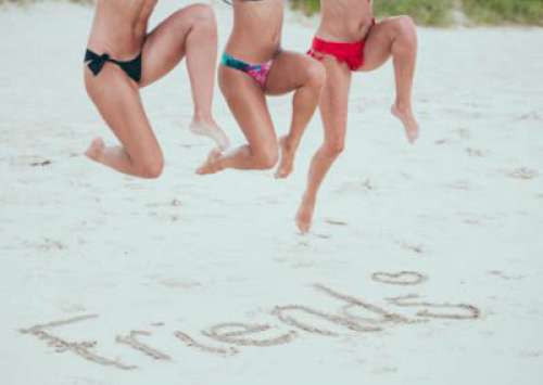 Girls In bikinis Jumping Over Friends On Beach