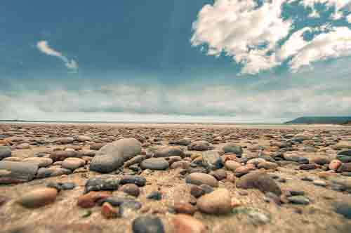 Dramatic Landscape Of Pebbles On Beach With Blue Sky And Clouds