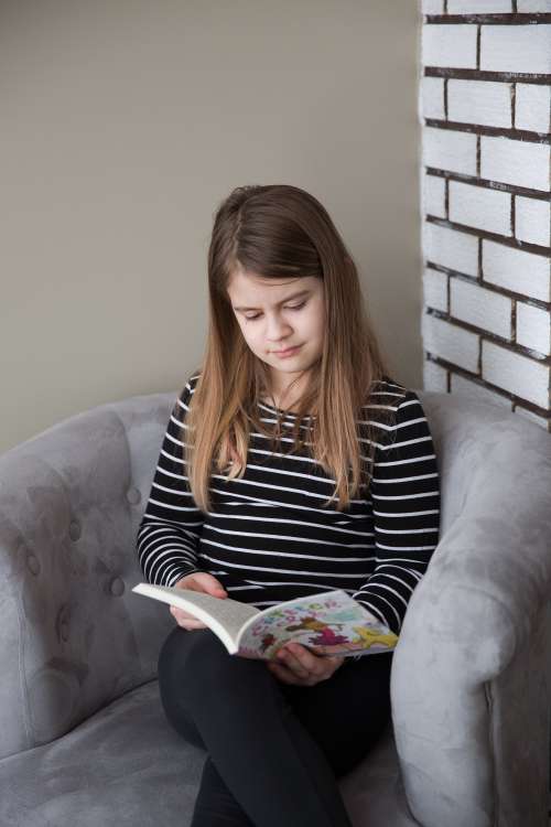 A Girl Sitting In A Chair Reads A Book Photo