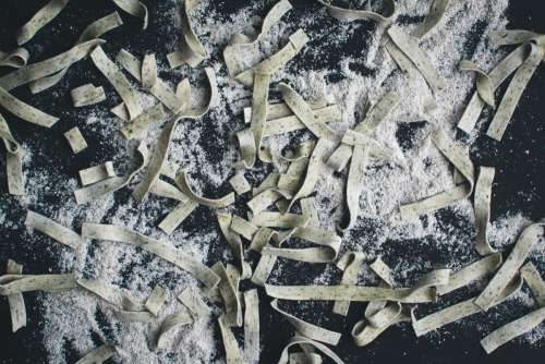 Pasta tagliatelle covered by flour on a black background