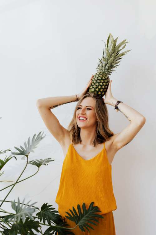 A beautiful smiling young woman is holding a pineapple