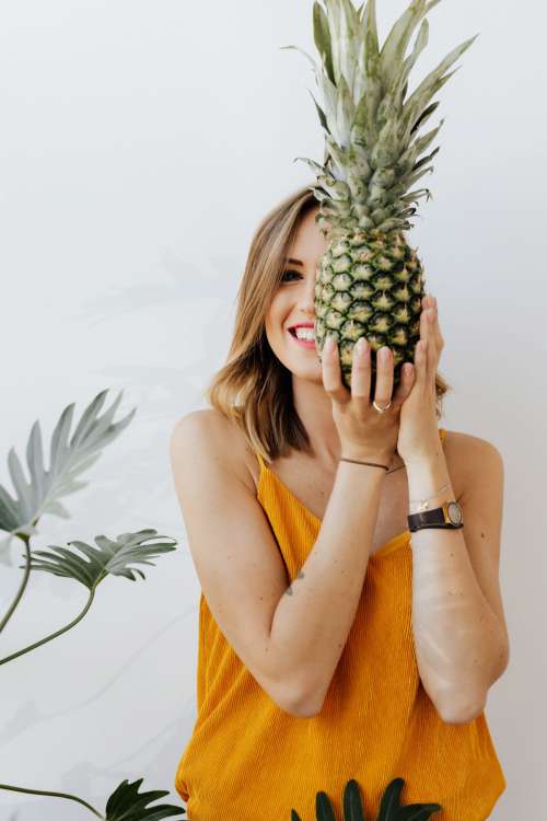 A beautiful smiling young woman is holding a pineapple