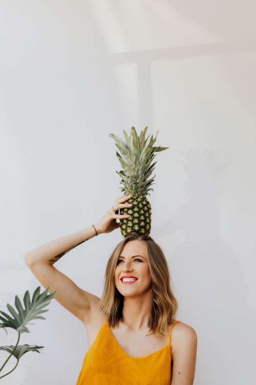 A beautiful smiling young woman is holding a pineapple